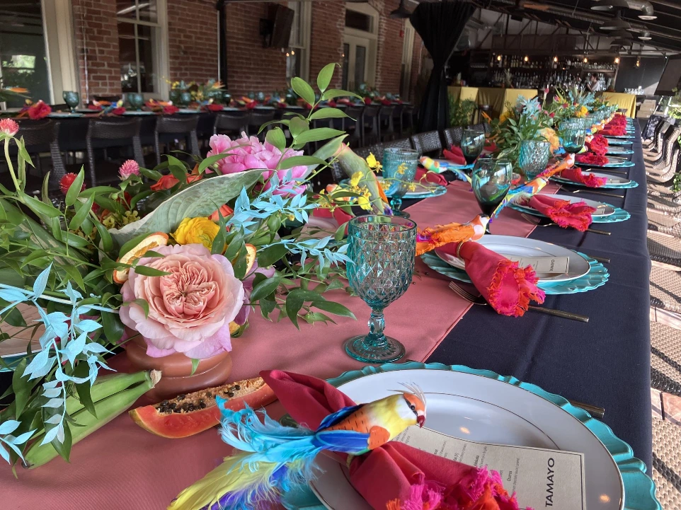 Long, color-forward tablescape with vibrant floral centerpieces featuring garden roses and mixed blooms, paired with teal glassware, bold linens, and layered place settings creating a rich, celebratory dining experience.